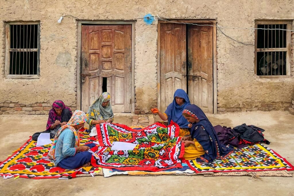 Sindhi women in Sukkur creating vibrant traditional textiles outdoors.