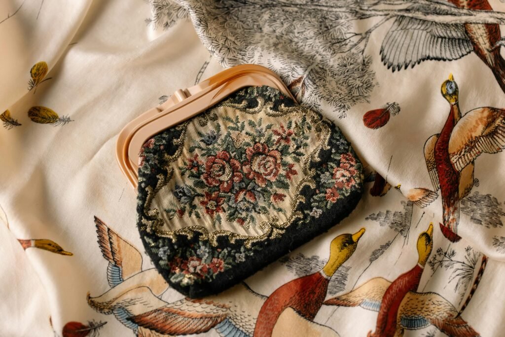 A vintage floral clutch bag resting on a patterned fabric with bird illustrations.