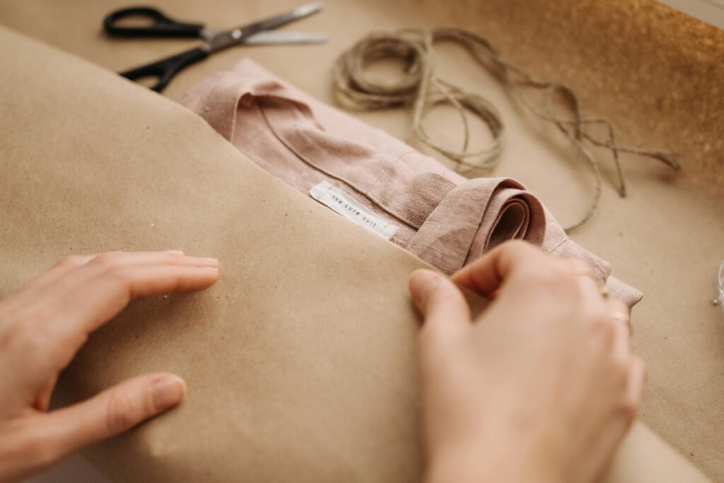 Close-up of hands wrapping a linen shirt with twine, showcasing craftsmanship and sustainable fashion.
